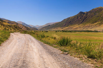 Dirt road leading towards mountains against clear sky