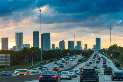 Traffic on road by buildings in city against sky