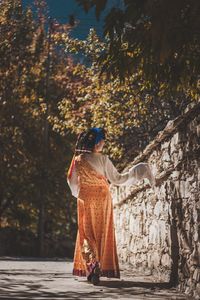 Rear view of woman standing by tree during autumn
