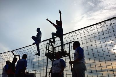 Low angle view of cheerful spectators by fence against sky