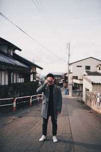 Full length portrait of young man standing in city against sky