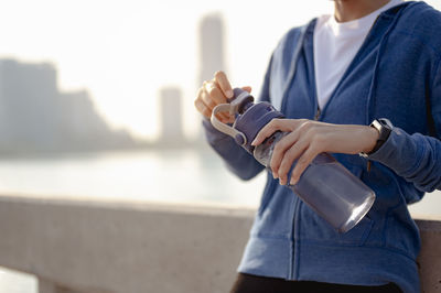 Midsection of woman holding water bottle while standing against railing