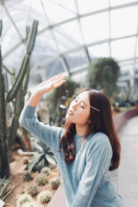 Young woman with eyes closed standing against plants in greenhouse