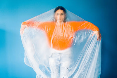 Woman covered in plastic standing against blue background