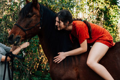 Young woman sitting on horse talking with friend in forest