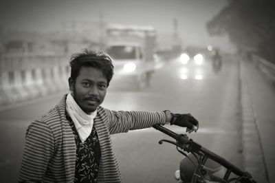 Portrait of young man standing by motorcycle on road at dusk