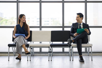 Full length of cheerful business people sitting on chair