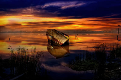 Scenic view of lake against dramatic sky during sunset