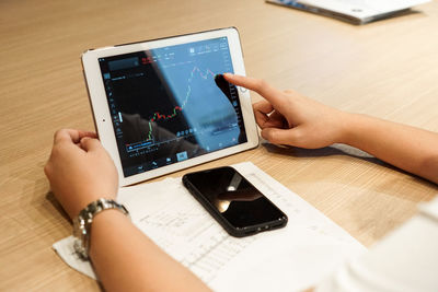 Woman using digital tablet by phone on table