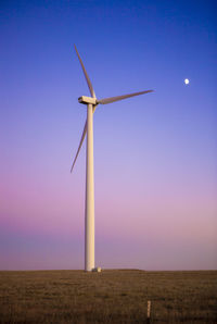 Wind turbine in field against blue sky at dusk