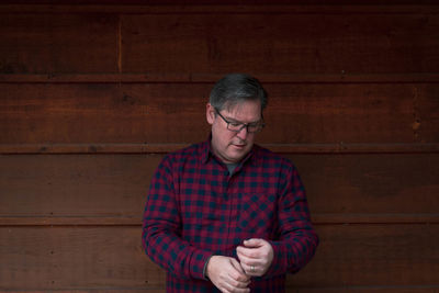 Mature man standing against wooden wall