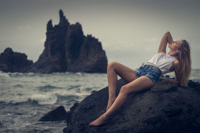 Woman lying on rock at beach against sky