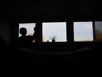 Silhouette woman against sky seen through window