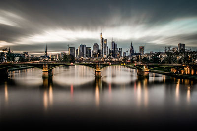 Illuminated buildings by river against sky in city