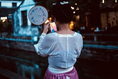 Rear view of woman holding umbrella standing in city