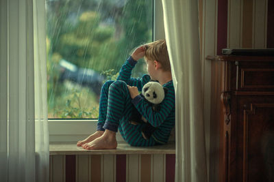 Full length of boy sitting at window
