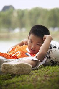 Full length of boy with soccer ball lying on field at park