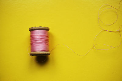 High angle view of thread spool over yellow background