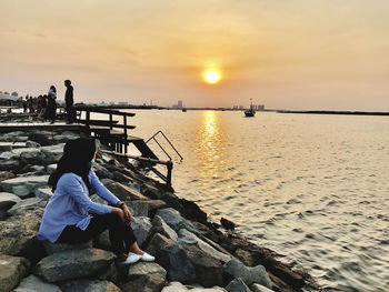 Rear view of woman sitting on beach against sky during sunset