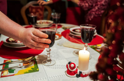 Hand toasting or serving a glass of dark red wine on table with tablecloth christmas celebration