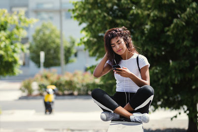 Full length of young woman using phone while sitting outdoors