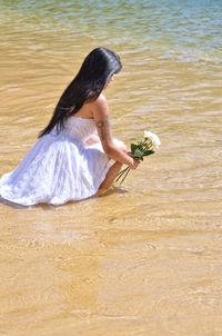 Side view of young woman with roses crouching at shore