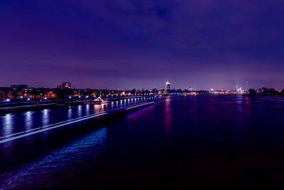 Illuminated city by river against sky at night