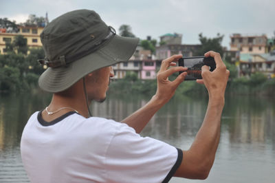 Back view of a male tourist taking photo of landscape with smartphone during cloudy weather 
