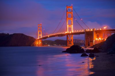 Illuminated golden gate bridge over bay against cloudy sky during dusk