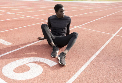 Sportsman contemplating while sitting on running track during sunny day