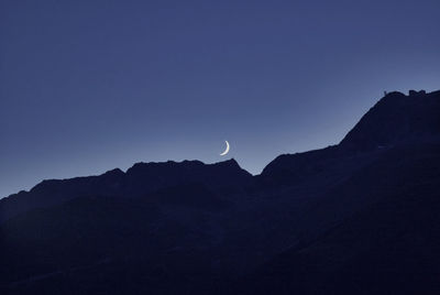 Low angle view of mountain against clear sky during sunset with descending moon