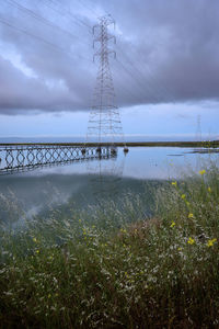 Electricity pylon by lake against sky