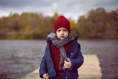 Child boy in knitted red hat and scarf in autumn on the street