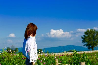Side view of woman by flowering field against blue sky