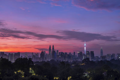 Illuminated buildings in city against sky during sunset