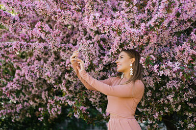 A happy smiling woman takes a selfie on her smartphone in a spring blooming garden, enjoying nature