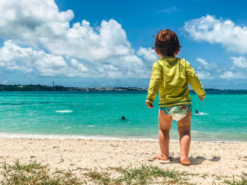 Rear view of boy standing at beach against sky