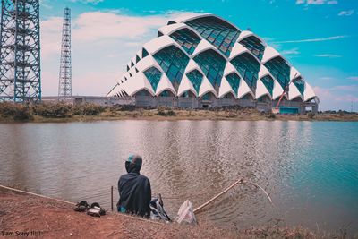 Rear view of men sitting on bridge over river against sky