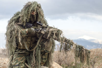 Army man in ghillie suit with rifle on field