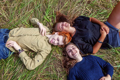 Top view group of three friends lying on grass in circle smiling and having fun together outdoors