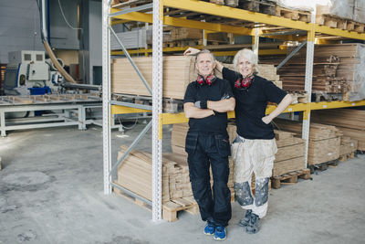 Full length portrait of smiling workers standing by rack in industry