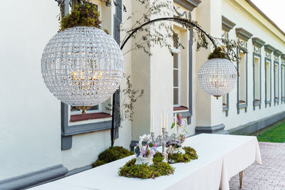 Festive table decorated with floral arrangement, candles and moss in courtyard under chandeliers