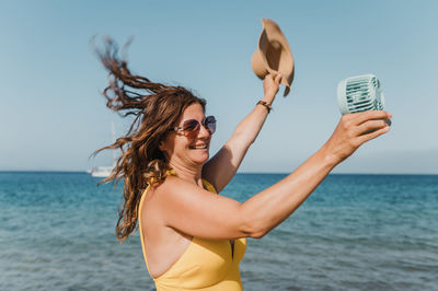 Rear view of young woman exercising in sea against sky