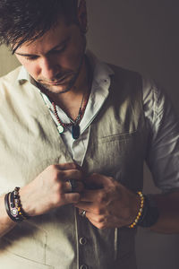 Thoughtful man buttoning waistcoat against wall