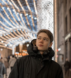 Close-up of teenage boy wearing warm clothing looking away in illuminated city