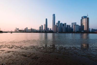 Sea by modern buildings against clear sky