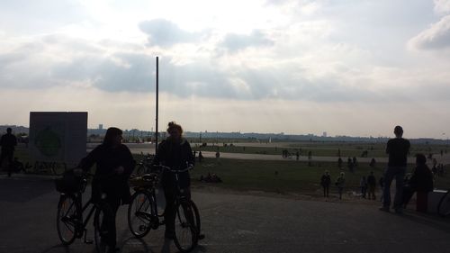 People cycling on road against cloudy sky