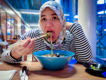 Portrait of woman eating noodle in bowl on table