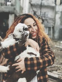 Smiling young woman embracing kid goat in winter