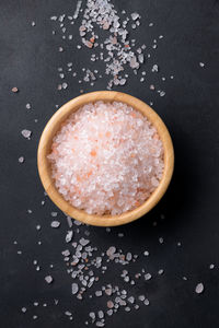 Pink himalayan salt in a wooden bowl with scattered salt on a black background, close up
